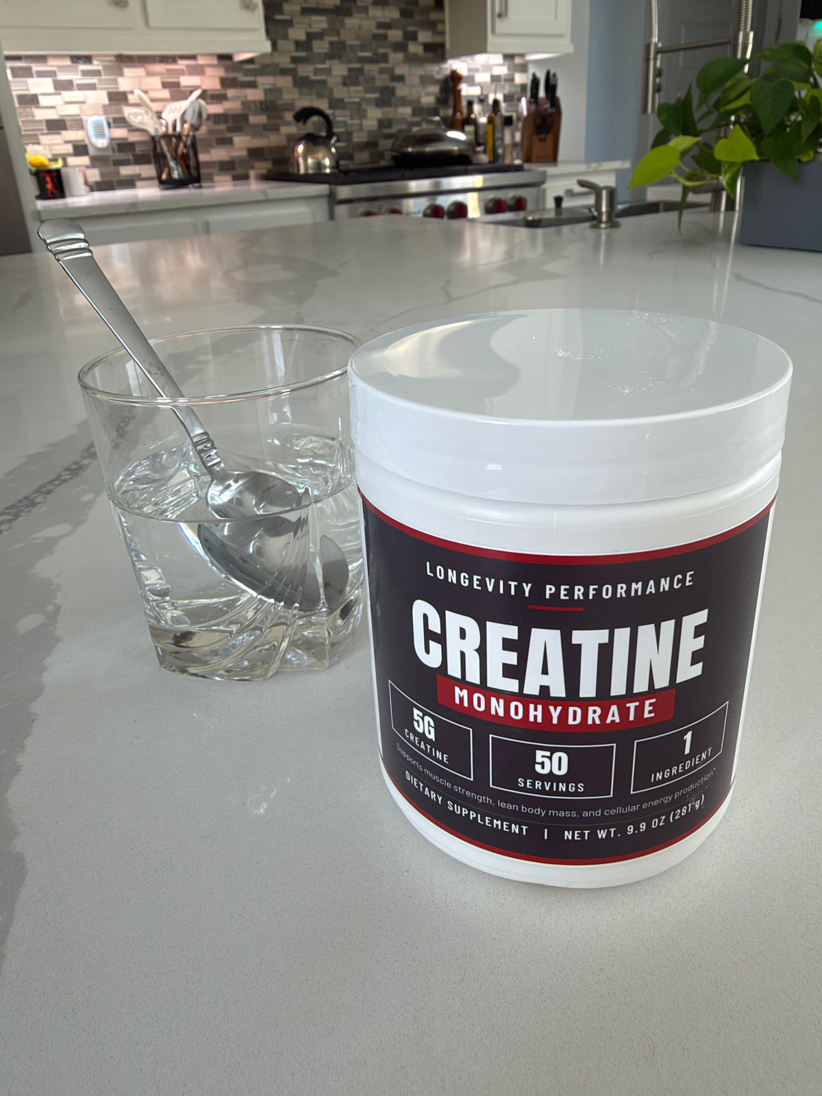 Longevity Performance Creatine Monohydrate on a kitchen island with a glass of water