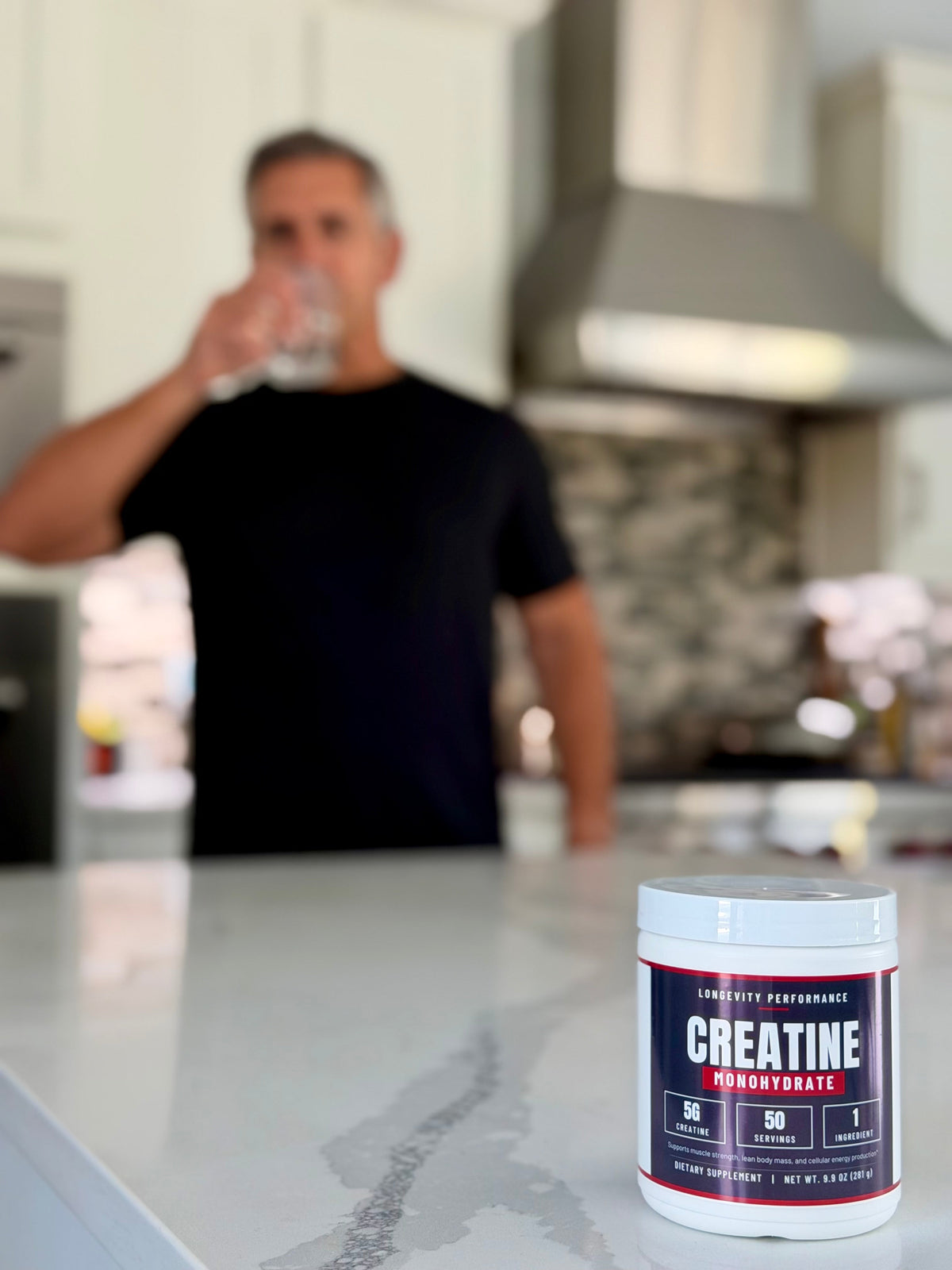 Longevity Performance Creatine Monohydrate on a kitchen counter with Luis drinking water in the background